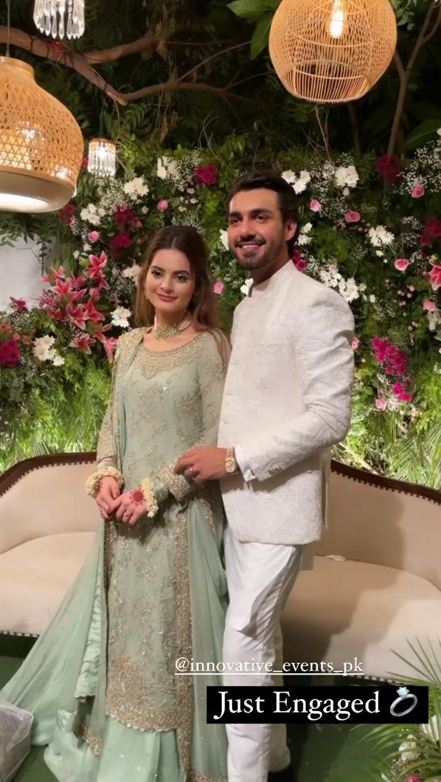 a man and woman standing next to each other in front of a flower covered wall