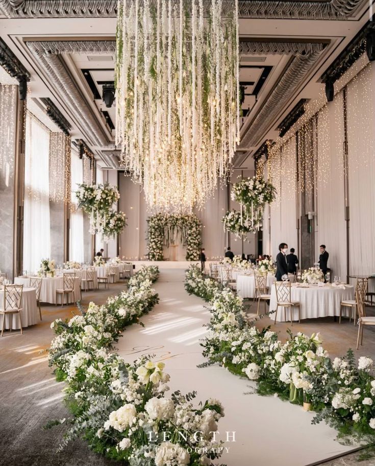 an elegant wedding setup with white flowers and greenery on the floor, chandeliers hanging from the ceiling