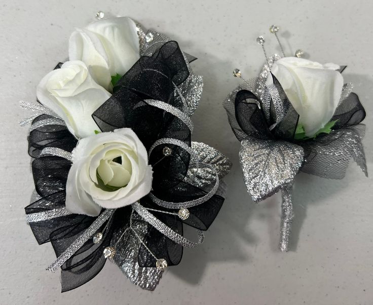 two white roses and black ribbon corsages with silver sequins on them