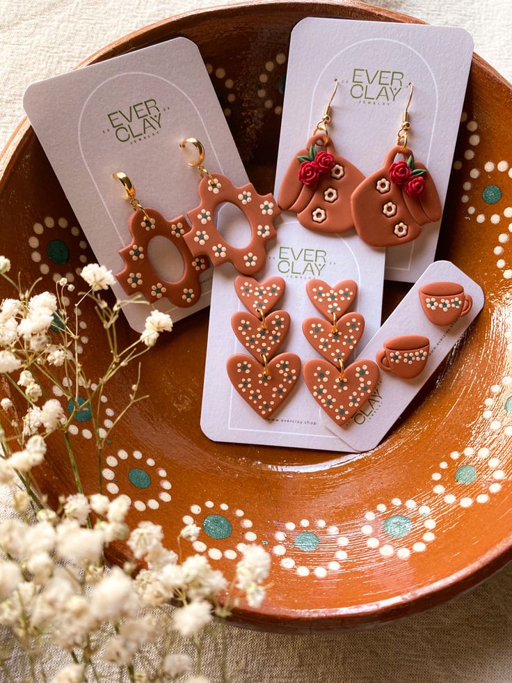 four gingerbread heart shaped earrings are on a plate next to some flowers and cards