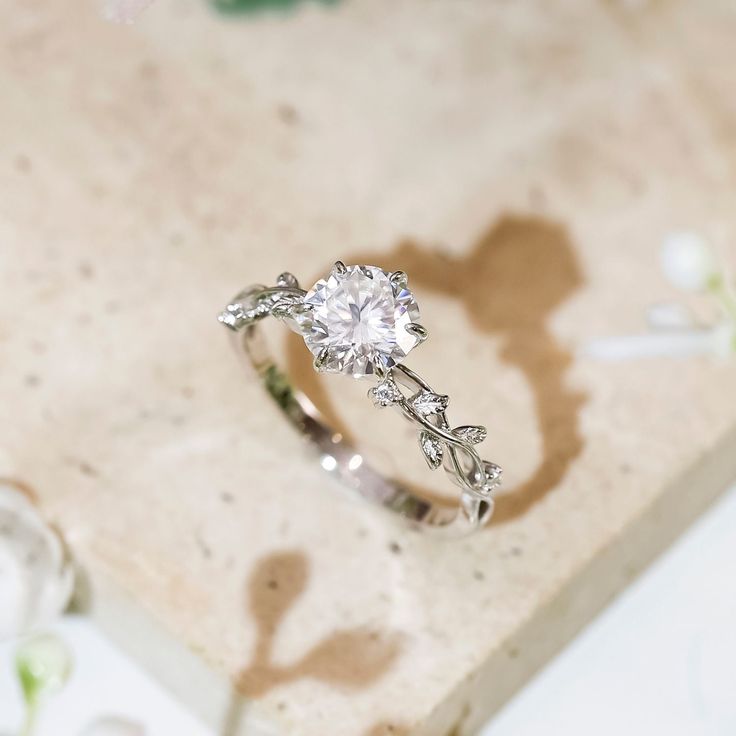 a diamond ring sitting on top of a marble slab with white flowers around it's edges