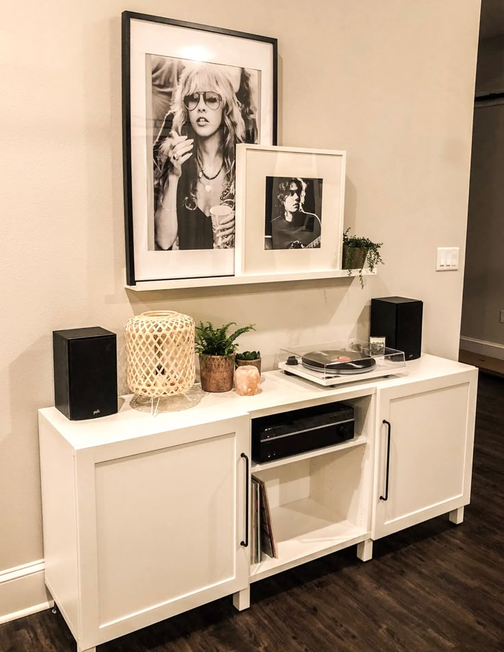 a white entertainment center with pictures on the wall and plants in vases next to it