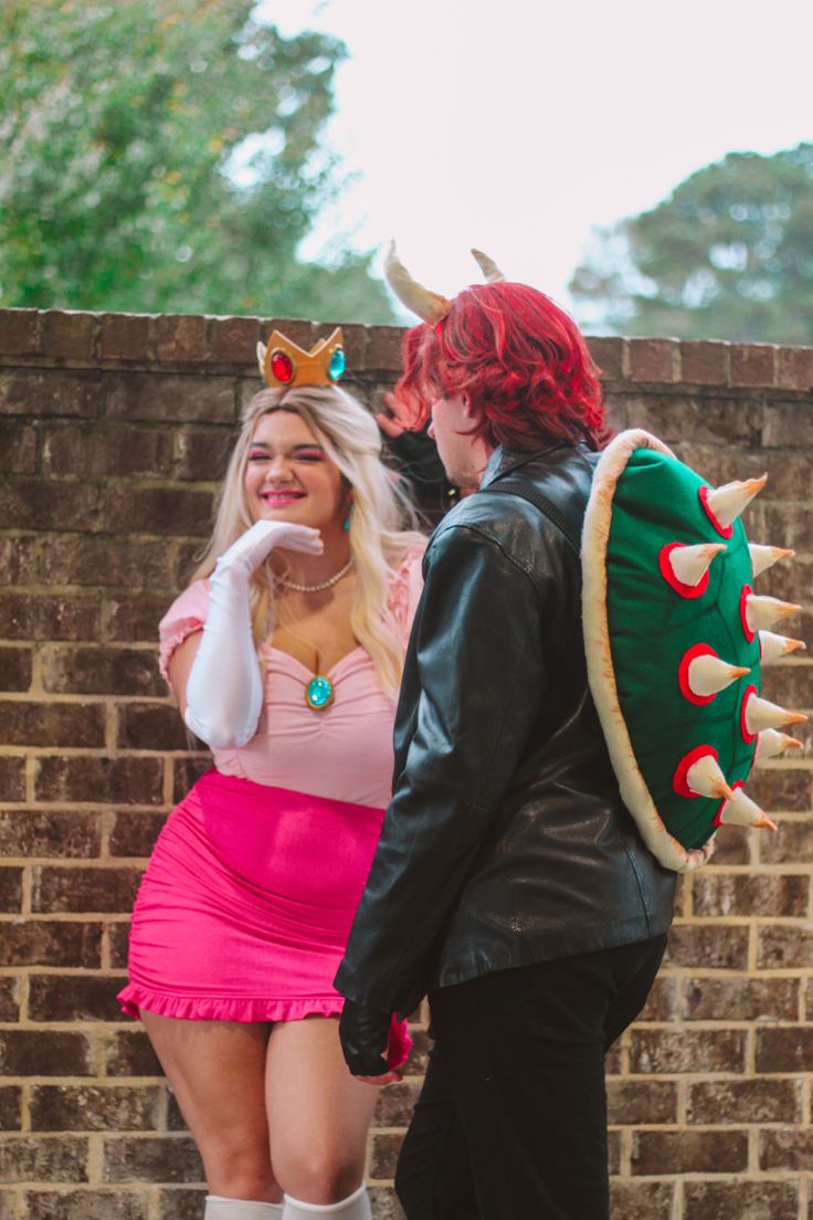 two people dressed in costumes standing next to each other near a brick wall and trees