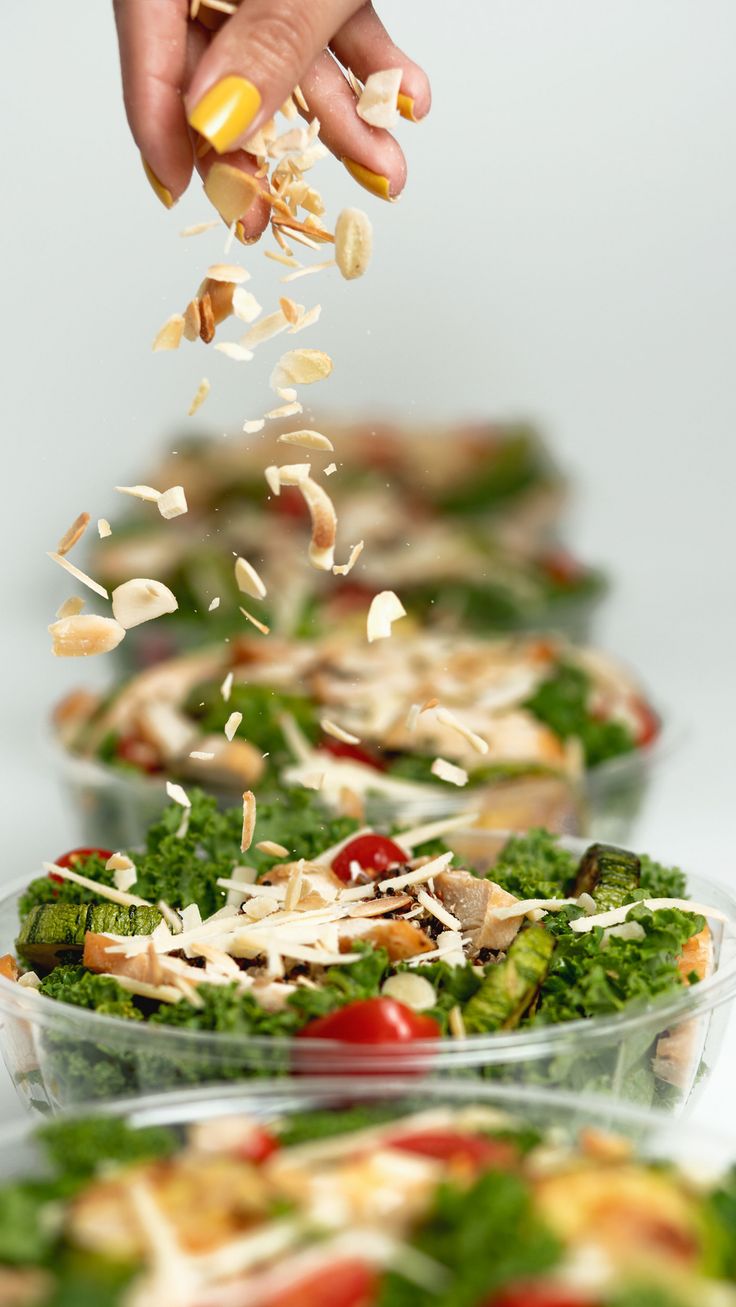 someone is sprinkling parmesan cheese onto a salad in plastic containers on the table