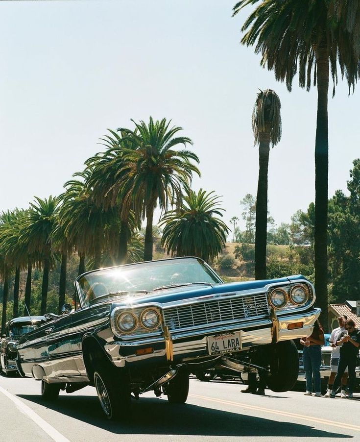 an old car driving down the road with palm trees in the background