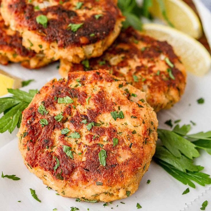 three crab cakes on a white plate with lemon wedges and cilantro garnish