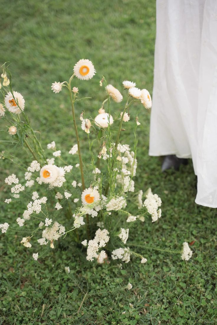 white daisies in a vase on the ground next to a bride's dress