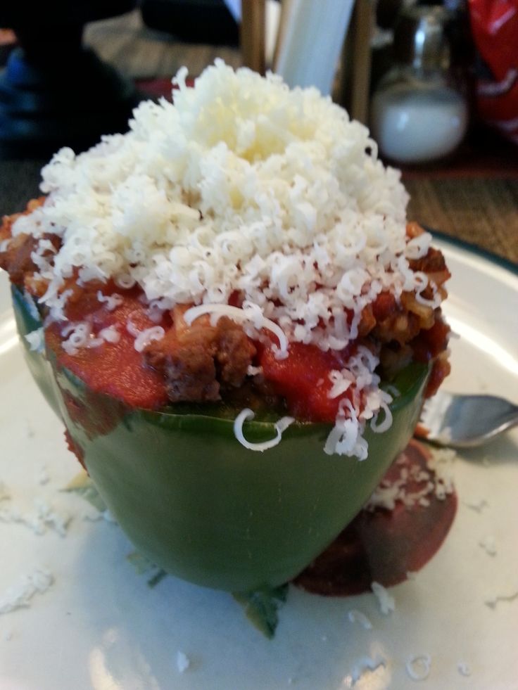 a white plate topped with a stuffed pepper covered in cheese and sauce next to a fork