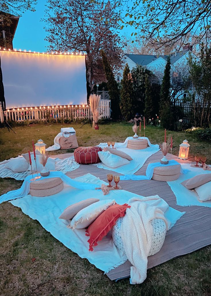 an outdoor movie set up with pillows, blankets and candles on the grass in front of a house