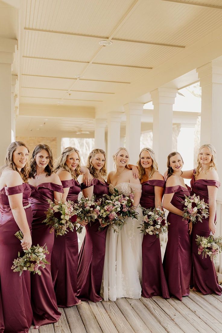 a group of women standing next to each other on a wooden floor holding bouquets