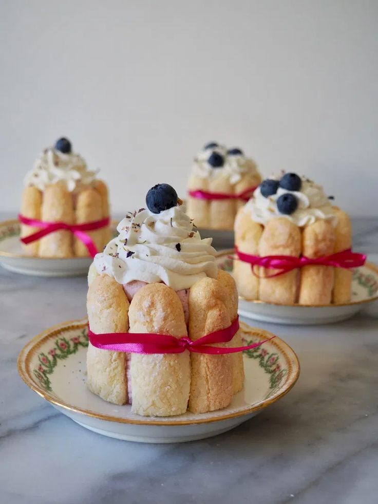 three small cakes with whipped cream and blueberries on top, tied in red ribbon