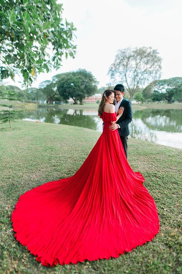 a man and woman standing next to each other in front of a lake wearing red dresses