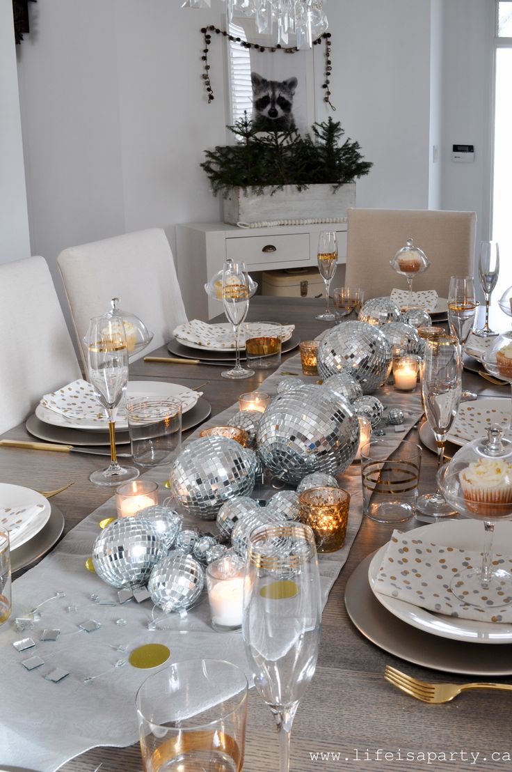 the table is set for christmas dinner with silver and gold decorations, candles and plates