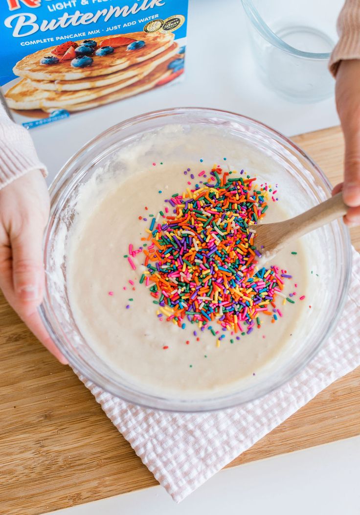 someone is spreading sprinkles on top of the cake batter in a glass bowl