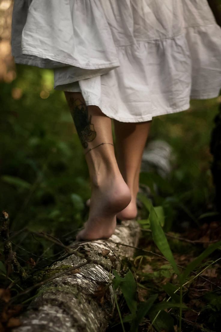 a woman with tattoos walking on a log in the woods