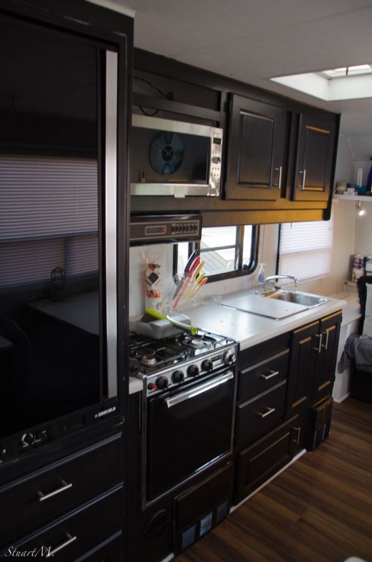 an rv kitchen with black cabinets and stainless steel stove top oven, microwave and dishwasher