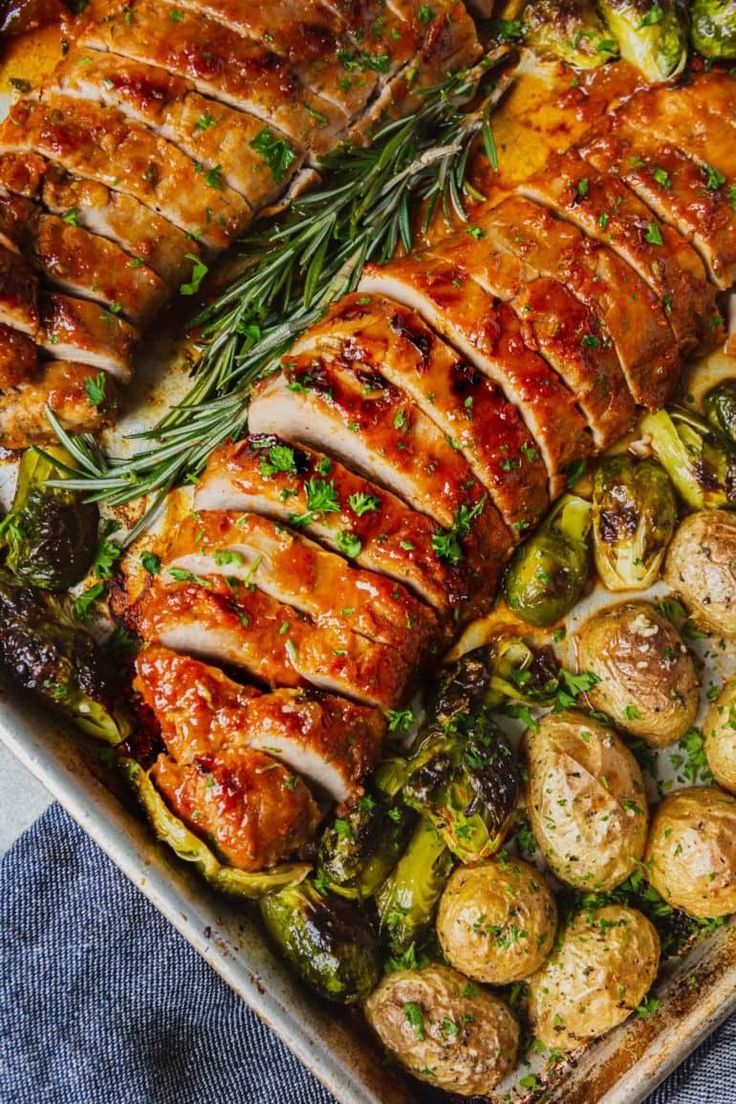 a pan filled with meat and vegetables on top of a blue table cloth next to a fork