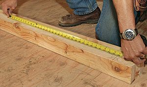 a man measuring the width of a piece of wood on top of a wooden floor