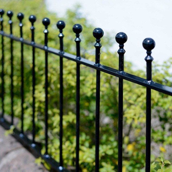 a close up of a black metal fence with green bushes in the background