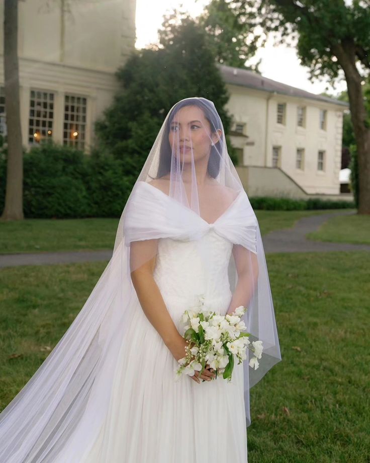 a woman in a wedding dress standing on the grass with her veil over her head