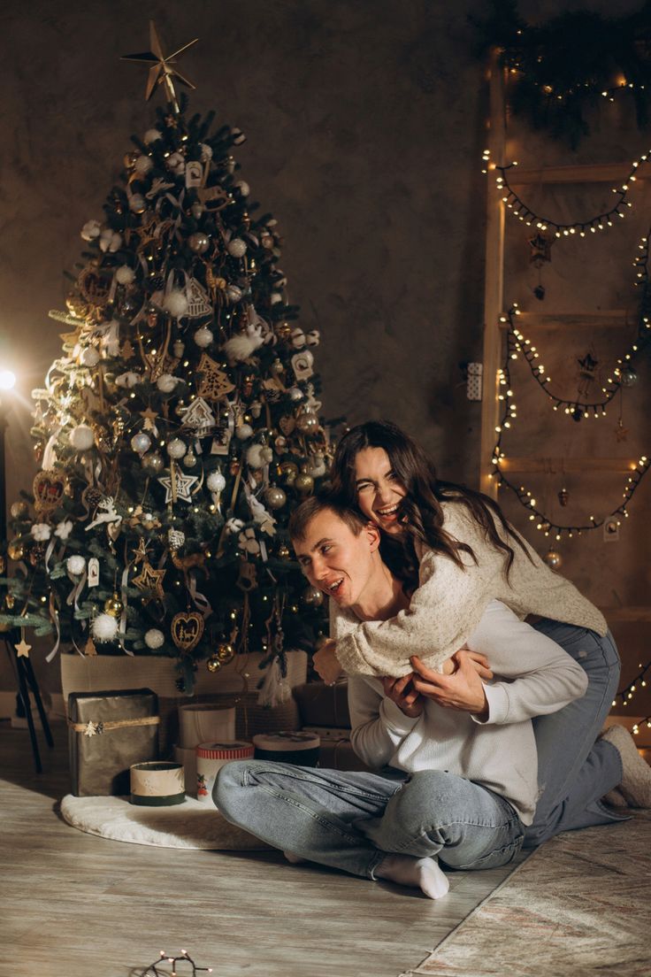 a man and woman sitting in front of a christmas tree with presents on the floor