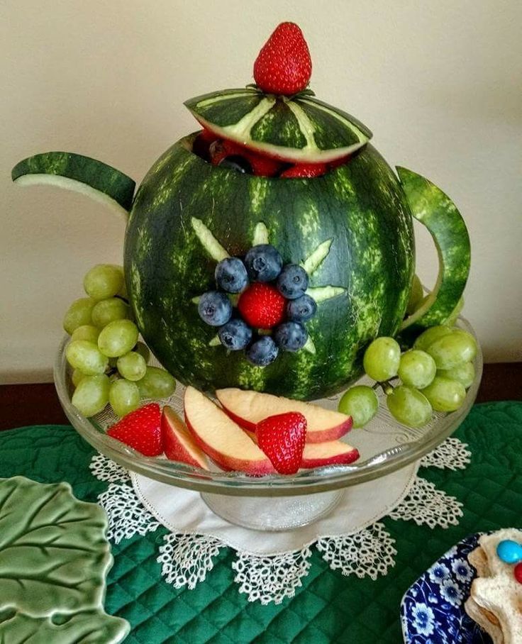 a watermelon shaped teapot with fruit in it on a green tablecloth