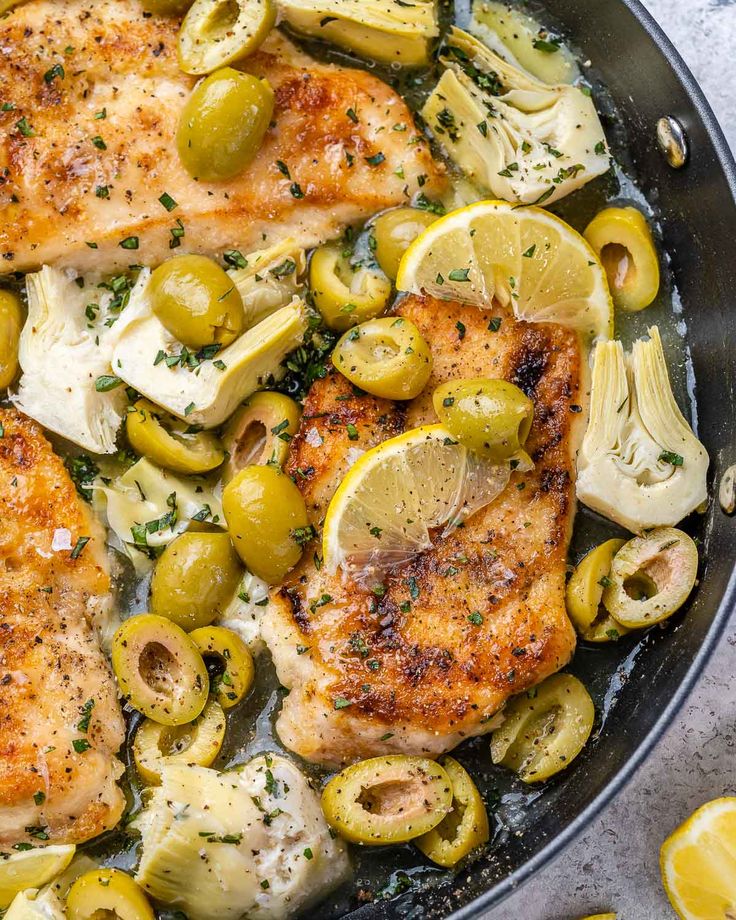 chicken and olives in a skillet with lemon wedges