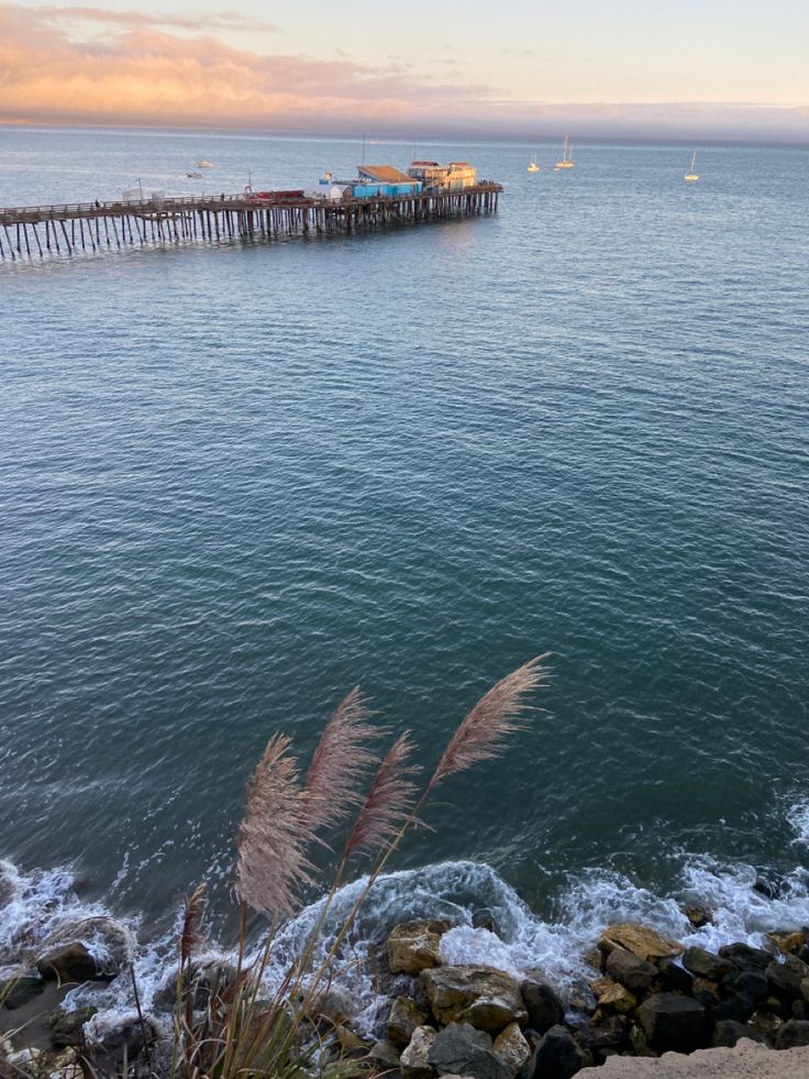 the water is calm and blue with waves coming in from the shore near a pier