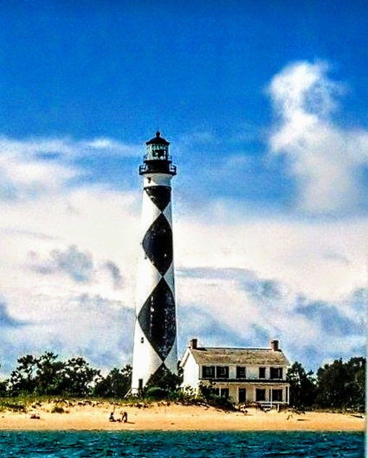 a lighthouse on an island in the middle of the ocean with people swimming around it