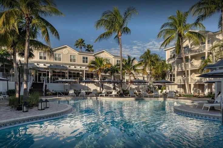 an outdoor swimming pool with lounge chairs and palm trees in the foreground, surrounded by apartment buildings