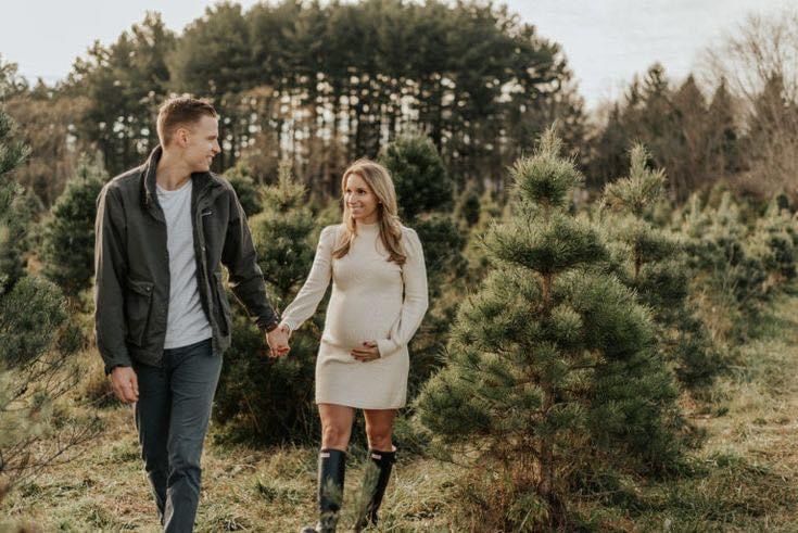 a pregnant couple walking through the woods holding hands