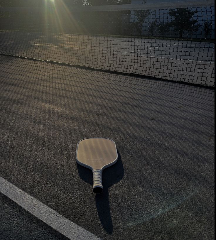 a tennis racquet laying on the ground in front of a net at sunset