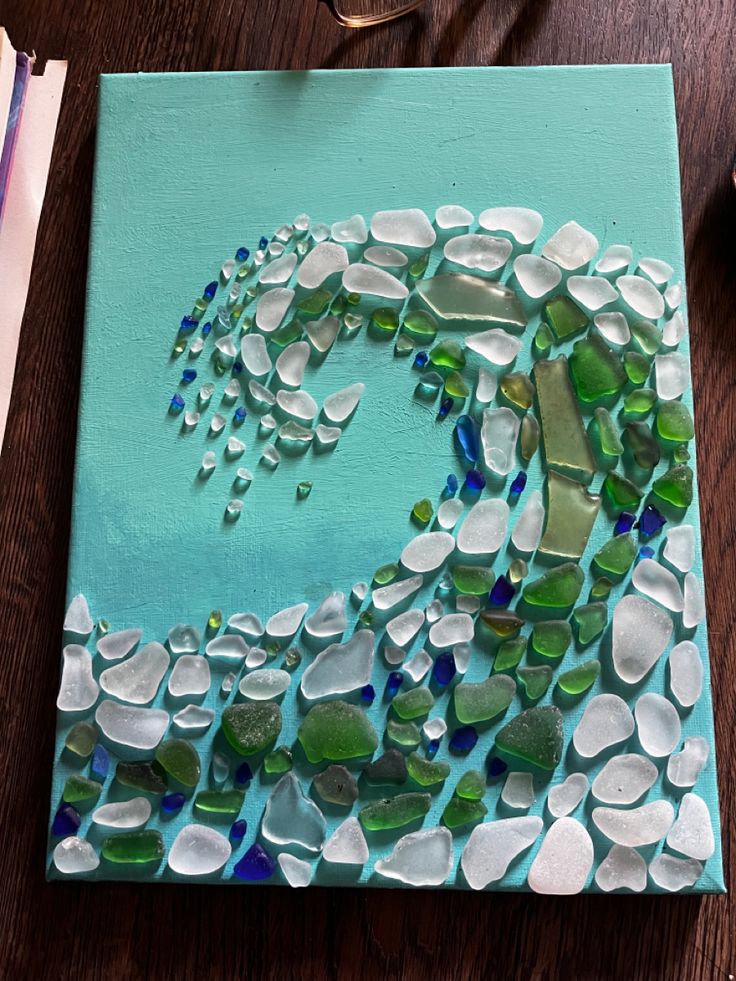 a painting made out of sea glass on a wooden table next to scissors and other items