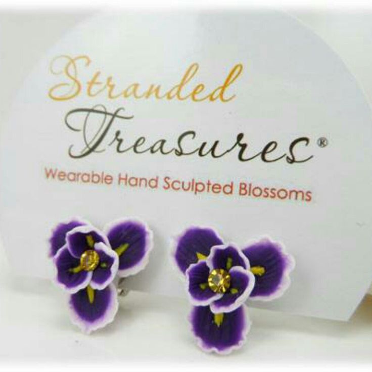 two purple and white flower shaped earrings sitting on top of a card with the words stranded treasures