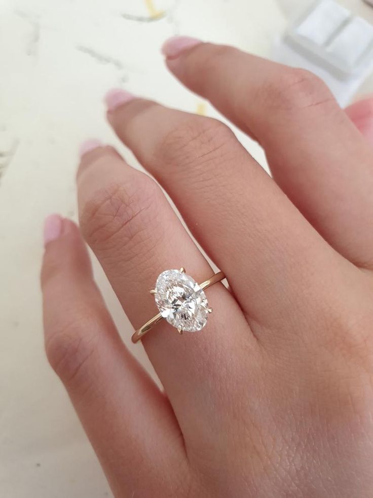 a woman's hand with a diamond ring on top of her finger and the other hand holding an engagement ring