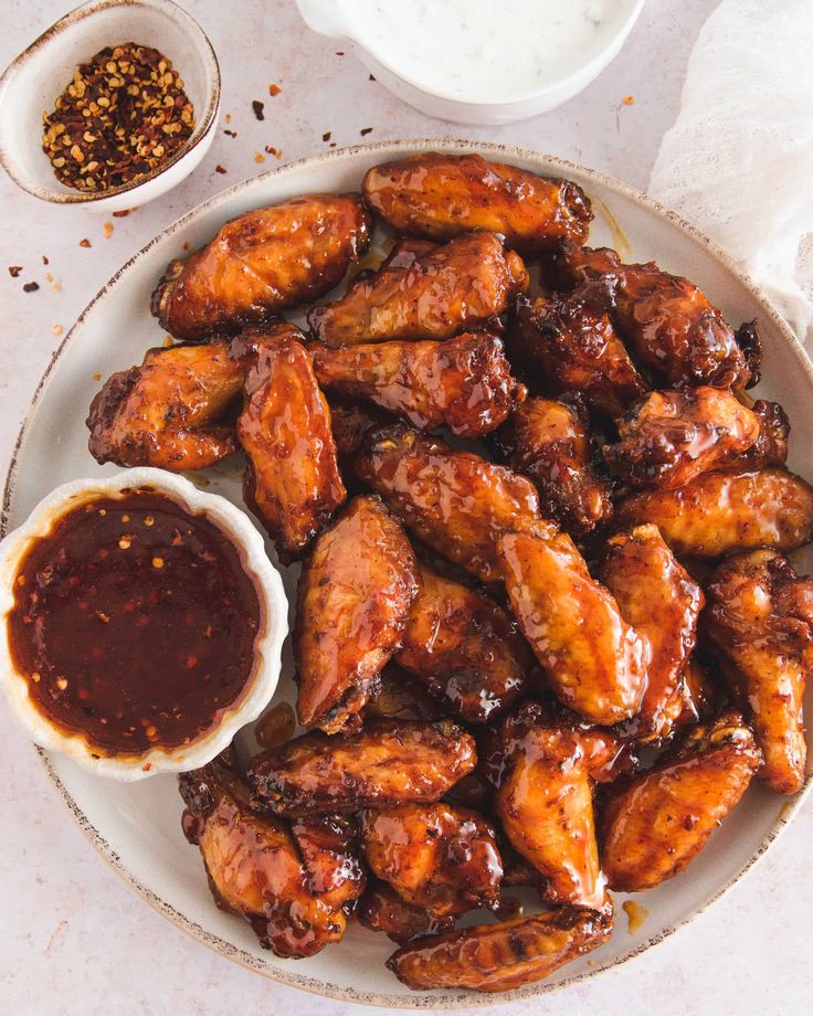 a plate full of chicken wings next to dipping sauce and seasoning on the side