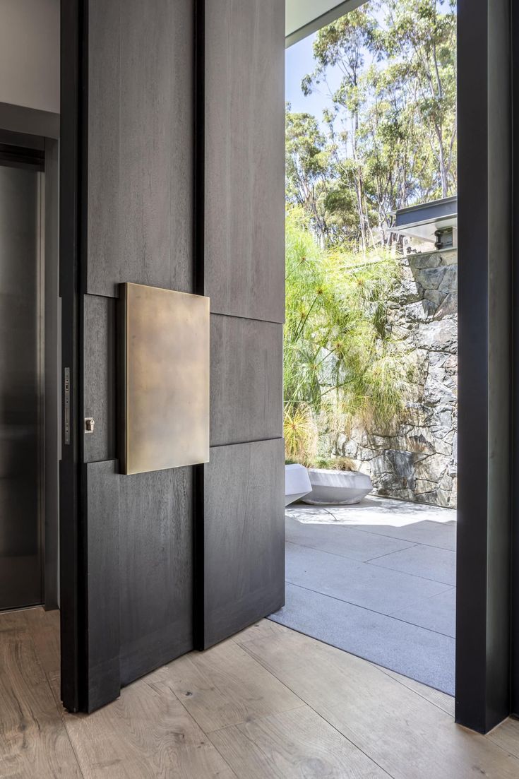 an open door leading to a patio with trees in the back ground and a stone wall behind it