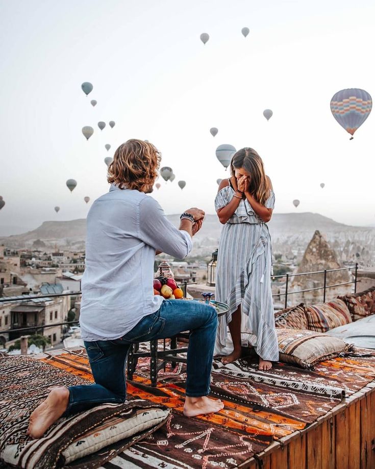 a man and woman sitting on top of a building with hot air balloons in the sky