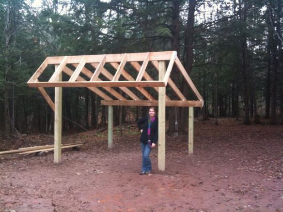 a woman standing under a wooden structure in the woods