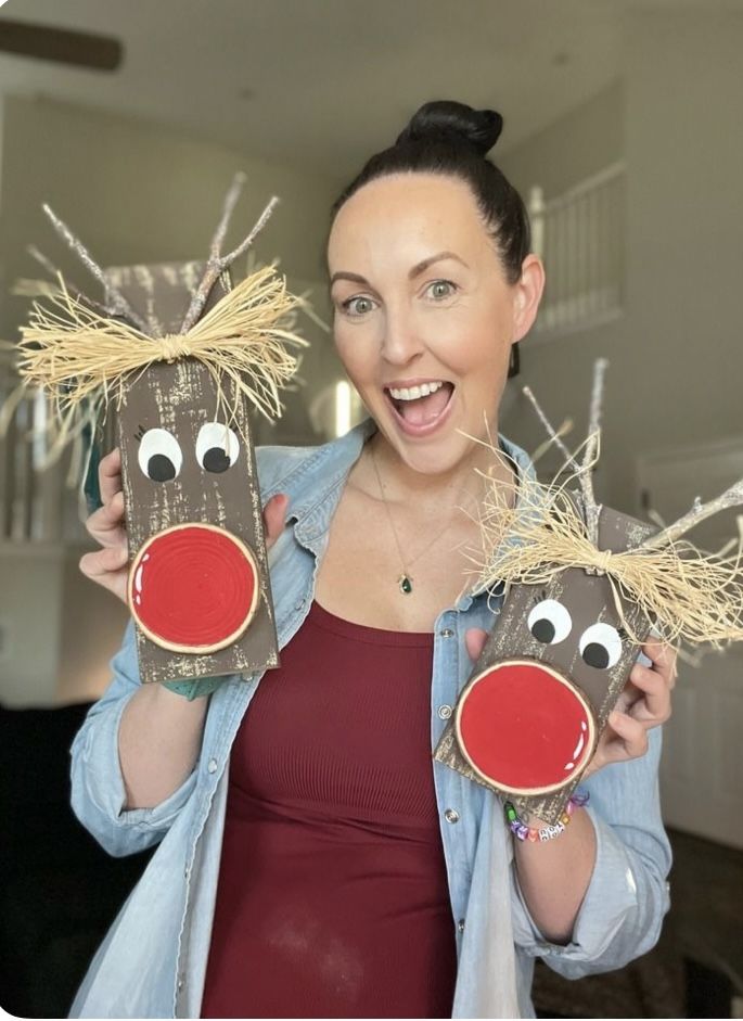 a woman holding two reindeer masks with hay on them