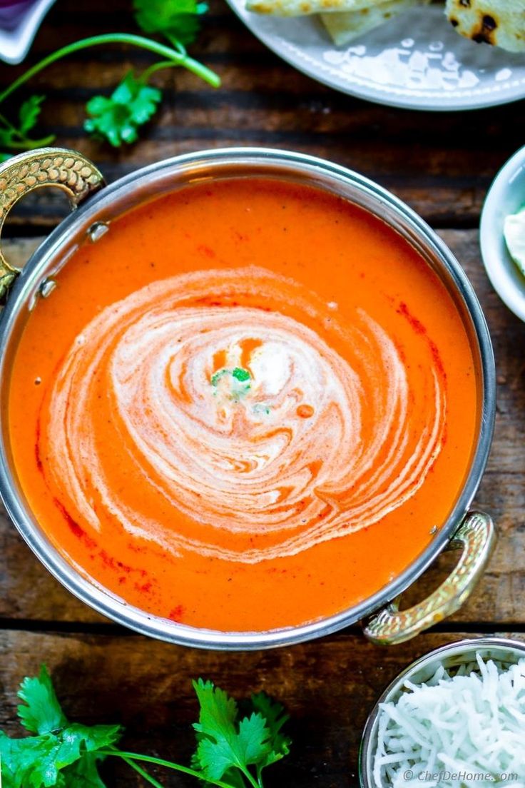 a bowl of tomato soup on a wooden table with bread and cilantro garnishes