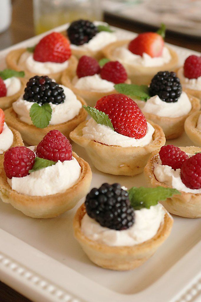 small desserts with berries and whipped cream on a white platter, ready to be eaten