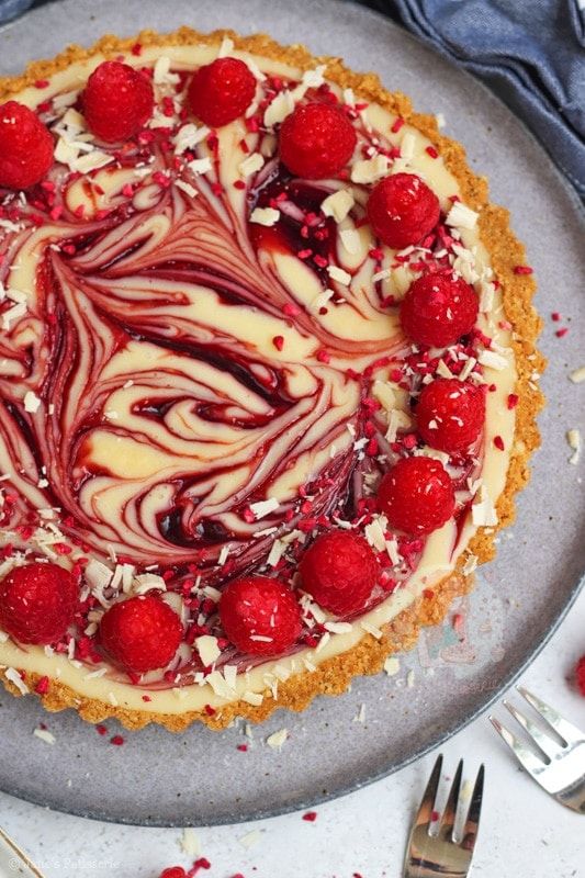 a cheesecake topped with raspberries on top of a metal tray next to silverware