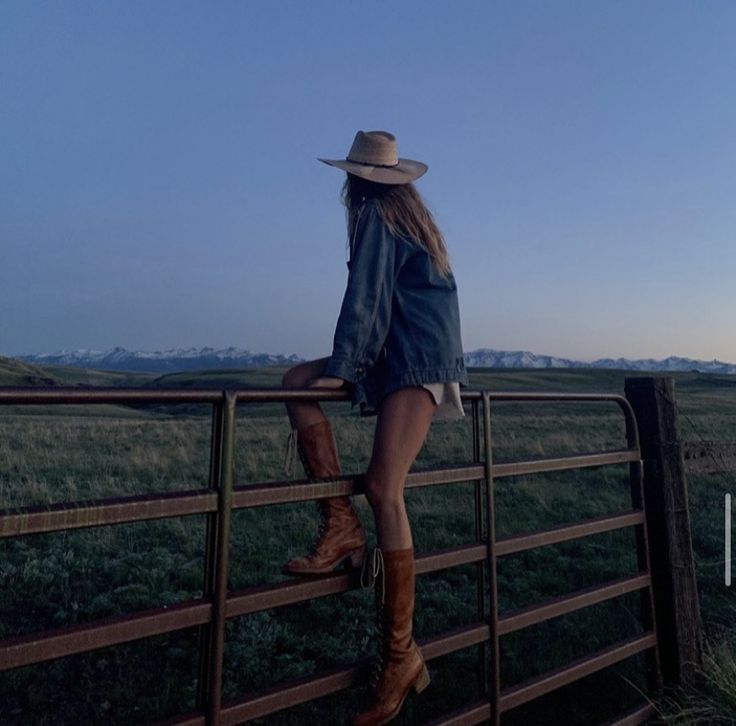 a woman in cowboy boots leaning on a fence