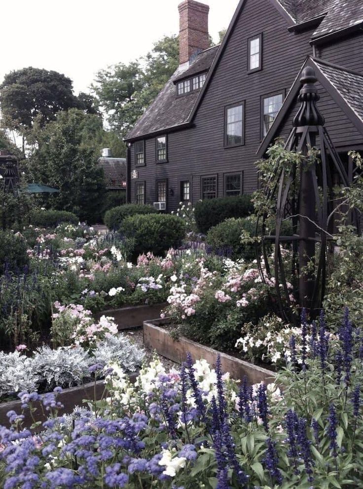 an old house with many flowers in the front and side garden on the other side