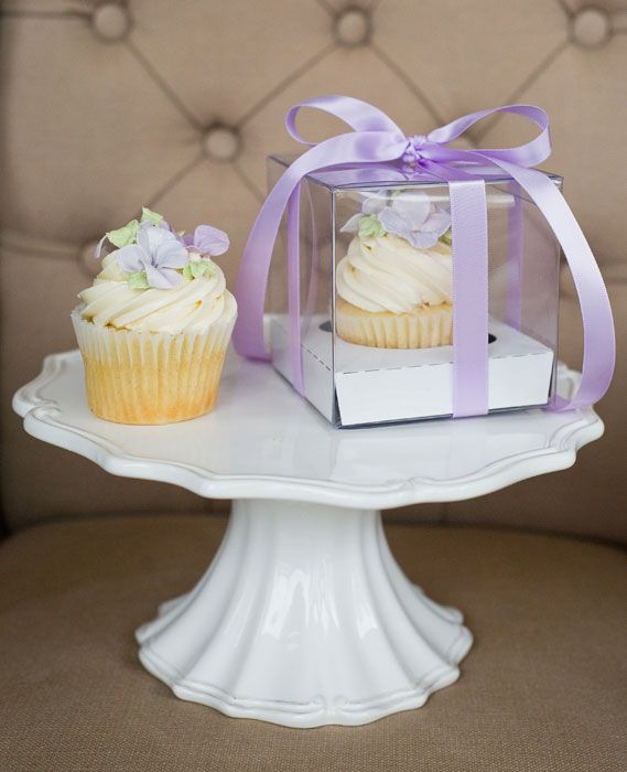 two cupcakes are sitting on a cake stand with a purple ribbon around it