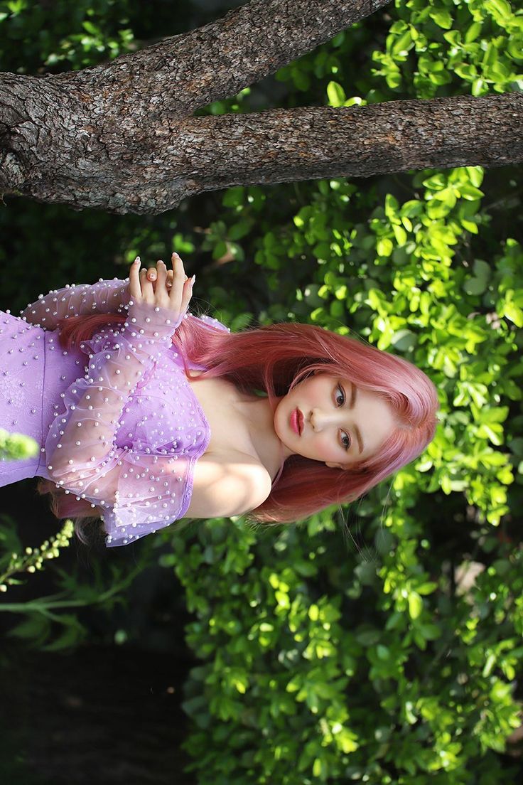 a woman in a purple dress is posing for the camera on a tree branch with green foliage behind her