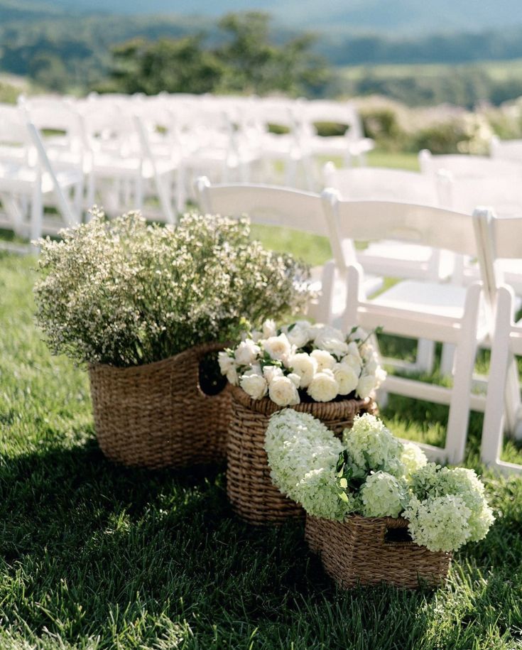 two wicker baskets filled with white flowers sit on the grass near rows of chairs