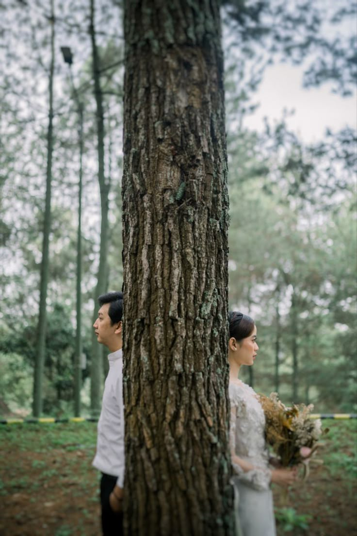 two people standing next to each other near a tree