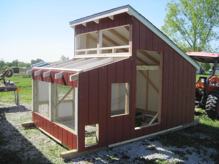 a small red chicken coop sitting on top of a grass covered field next to a tractor